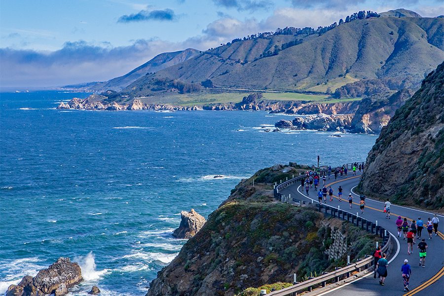 A view of Big Sur International Marathon runners running on a bridge with green mountains in the distance